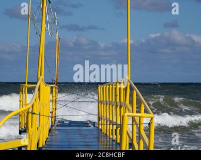 a blue wooden footbridge with yellow railings leads into the Baltic Sea Stock Photo