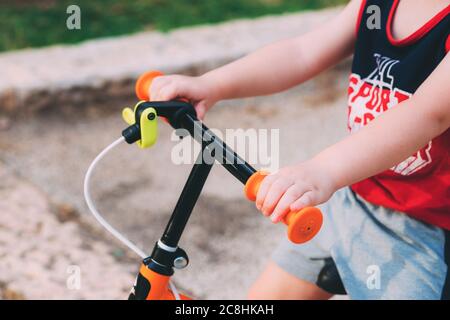 Blurred child sits on a bicycle. Father's day. Child's hands on the hand of an orange bike for children. Little pens. Little son rides a bicycle Stock Photo