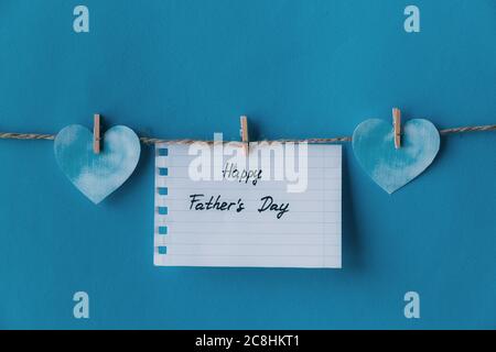 White notebook in line paper greeting card with black handwritten lettering happy fathers day hanging on brown rope with clothespins isolated on blue Stock Photo