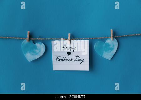White notebook in line paper greeting card with black handwritten lettering happy fathers day hanging on brown rope with clothespins isolated on blue Stock Photo