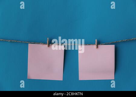 Two pink sheets of paper with place for text hanging on rope isolated blue background. To do list. Pink sticky notes with cloth pegs. Pink notes paper Stock Photo