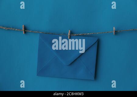 One closed blue envelope hanging on rope isolated blue background. Write a letter to a friend. Postal envelope. Gift envelope for postcards. Stock Photo