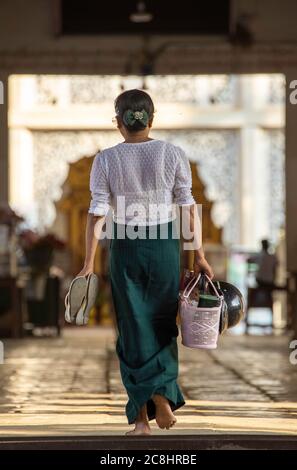 A Burmese woman walking carrying shoes and baskets in the temple area. Taking off shoes in the temple area is a tradition of Burmese people in order t Stock Photo