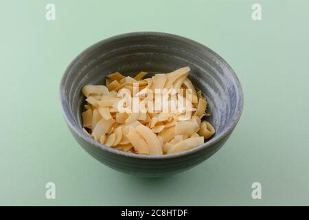 Salted caramel coconut chips in ceramic snack bowl on green background Stock Photo