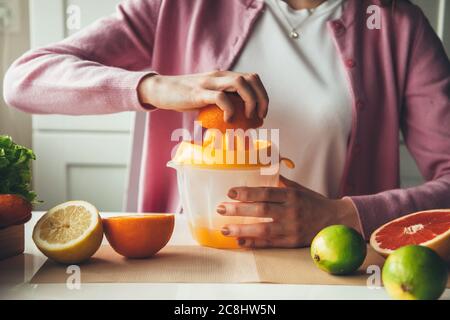 Close up photo of a caucasian woman with healthy habits squeezing juice from oranges and lemons in the kitchen Stock Photo