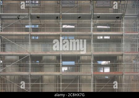 Building facade renovation, old house reconstruction, repair. Scaffold in front of building facade covered with transparent fabric Stock Photo