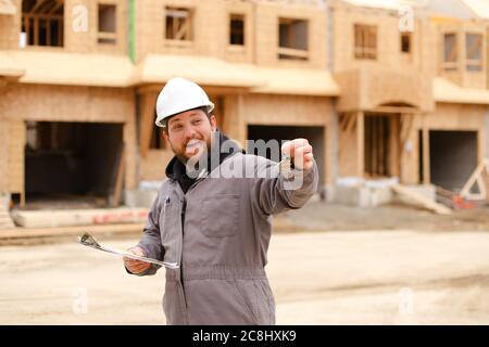 European foreman giving apartment keys and holding drawing plan in notebook. Stock Photo