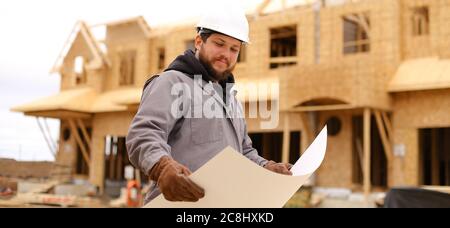 Banner of builder holding architectural drawing plan on paper at construction site. Stock Photo
