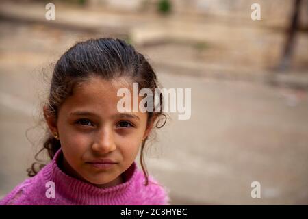 Tartus, Syria 03/27/2010: A close up face portrait of an 8 years old brunette Syrian girl at a poor neighborhood in Tartus. She has old torn pink pull Stock Photo