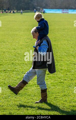 Oxford ,UK 03/19/2011: An elderly grandfather is carrying his grandson on his shoulders as they both stroll through the park in a sunny afternoon. The Stock Photo