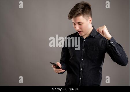 Portrait of serious stylish attractive man dressed with a casual black shirt using mobile applications text messages gesturing happy face on cellphone Stock Photo