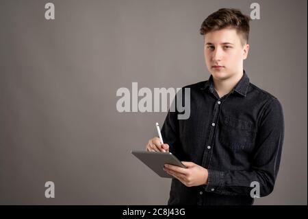 Portrait of serious stylish attractive man dressed with a casual black shirt taking notes, looking at the camera isolated on gray background with copy Stock Photo