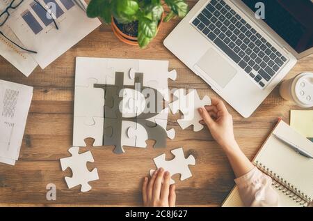 Woman sitting at her workplace in the office. Top view close-up. Businessman is trying to connect couple puzzle piece. Symbol of bitcoins. Concept of Stock Photo