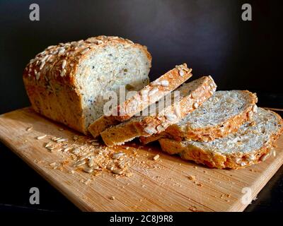 Loaf of German traditional multi-cereal bread Vollkornbrot, partially cut into slices on a wooden cutting board, knife with a wooden handle. Natural Stock Photo