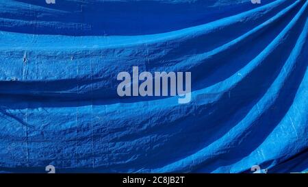Folds of rumpled plastic fabric texture with copy space. Old blue drapery background with diagonal wavy structure Stock Photo