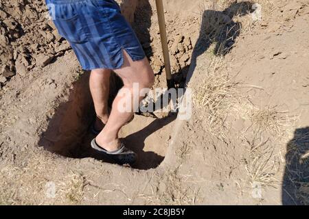 man digs a deep grave. gravedigger digs a grave with a shovel in a cemetery. Stock Photo