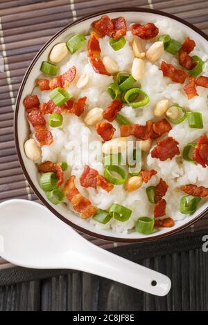 Rice porridge with bacon, peanuts and green onions close-up in a bowl on the table. Vertical top view from above Stock Photo