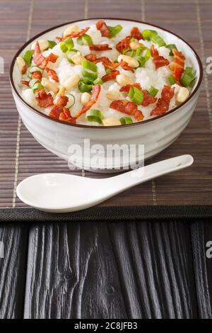 Chinese cooking, congee (jook) boiling jasmine rice with a lot of water over low heat with the addition of bacon, peanuts and green onions close-up in Stock Photo