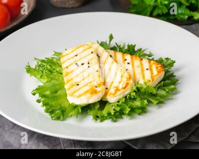 Grilled Halloumi, fried cheese with lettuce salad. Balanced diet, white plate on dark background, side view Stock Photo