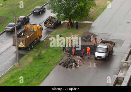 Saint Petersburg, Russia - July 28, 2019: Workers in orange overalls doing road work on laying of asphalt in rainy weather the view from the top Stock Photo