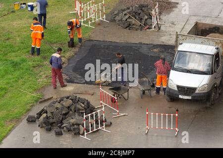 Saint Petersburg, Russia - July 28, 2019: Guest workers in overalls perform road works on laying asphalt in rainy weather Stock Photo