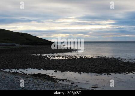 Sun rays coming through clouds onto the ocean, seen from a rocky beach in Trefor, North Wales Stock Photo
