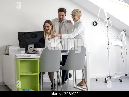 Office with three caucasian doctor colleagues looking at the computer screen behind the desk Stock Photo