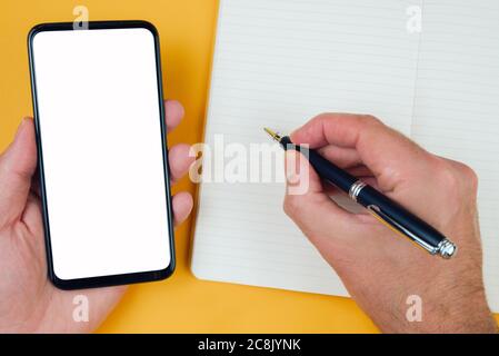 top view of person taking notes on paper while using smartphone, template with copy space Stock Photo