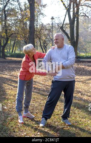 Vertical shot of a Caucasian senior woman helping her husband while jogging in a park together Stock Photo