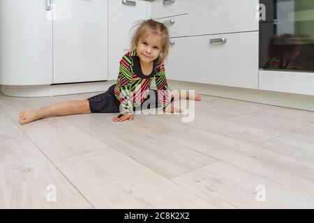 beautiful girl 4 years old in a gymnastic leotard is engaged in gymnastics at home in the kitchen. sitting on twine, copy space Stock Photo