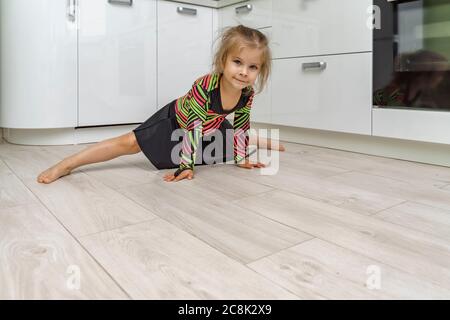 beautiful girl 4 years old in a gymnastic leotard is engaged in gymnastics at home in the kitchen. Stock Photo