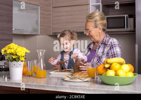 Little girl preparing pancakes with chocolate cream in the kitchen with her grandmother Stock Photo