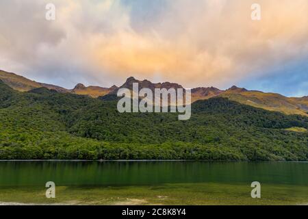 Forests and mountains surrounding North Mavora Lake at sunset on a cloudy day. Stock Photo