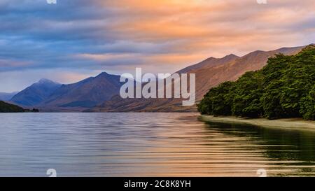 North Mavora Lake surrounded by forests with mountains in the background at sunset on a cloudy day. Stock Photo