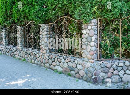 beautiful patterned wrought iron fence with stone pillars on sunny summer day Stock Photo
