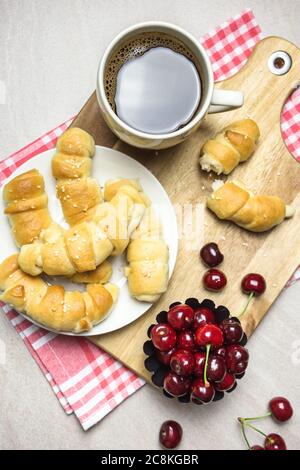 Breakfast with homemade croissants, coffee and sweet cherries on light textured background, top view. Stock Photo