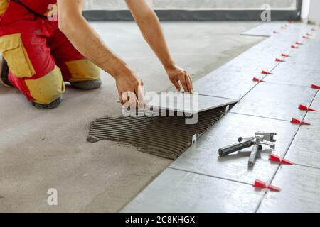 Ceramic Tiles. Tiler placing ceramic wall tile in position over adhesive with lash tile leveling system - Image Stock Photo