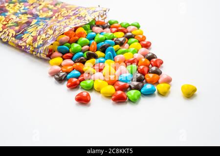 Small multi colored in a shape of a heart candies are scattered from of a festive beautiful bag. On a white background with place for text. Stock Photo