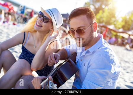 Closeup shot of a man next to the woman playing guitar on the beach Stock Photo