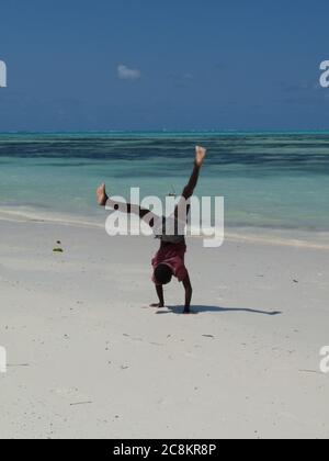 Young black boy doing handstand on white sand beach, Zanzibar,Tanzania Stock Photo