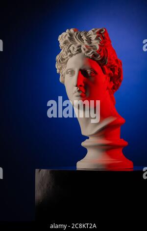 White plaster statue of a bust of Apollo Belvedere in red light on a blue background Stock Photo