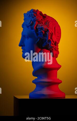 Plaster statue of a bust of Apollo Belvedere in red and blue light on a yellow background Stock Photo