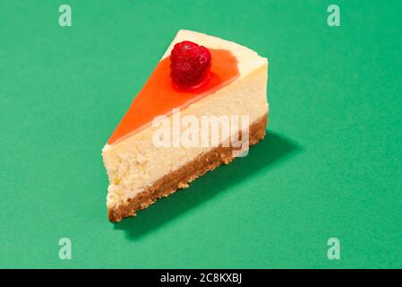 Cheesecake slice with raspberry syrup and cracker crust isolated on a green seamless background, in bright light. Close-up of a slice of cheesecake. Stock Photo