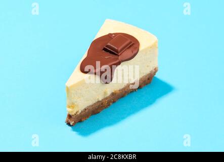 Cheesecake slice with melted chocolate and cracker crust, on a blue background. Close-up of a slice of cheesecake with dripping chocolate sauce. Stock Photo