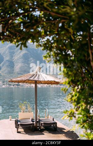Lounges on the dock near the sea under a thatched beach umbrella. Stock Photo