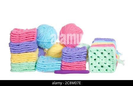 Piles of colorful hand crochet granny squares with balls of yarn piled behind, crochet hook laying in front. Isolated on white background. Stock Photo