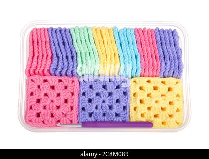 Piles of colorful hand crochet granny squares in a box, some lined up on side, others facing pattern upwards laying in a plastic box, isolated on whit Stock Photo