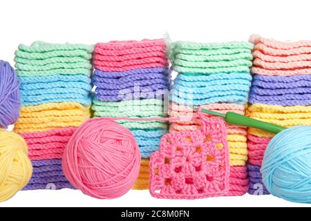 Close up on piles of colorful hand crochet granny squares with balls of yarn piled behind, crochet hook laying in front with partially completed grann Stock Photo