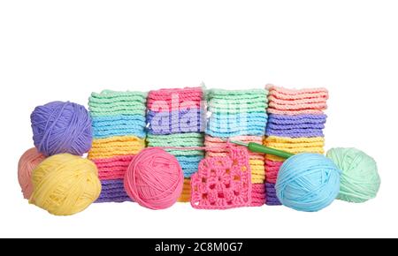 Piles of colorful hand crochet granny squares with balls of yarn piled behind, crochet hook laying in front with partially completed granny square. Is Stock Photo