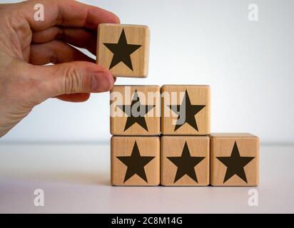 Male hand placing a cube with star sign on top of a pyramid. Beautiful white background. Quality and luxury conceptual image. Stock Photo